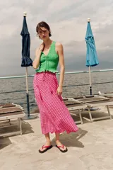 Falda midi con silueta evasé y estampado de cuadros en tonos fucsia y blanco. Presenta cintura elástica con lazo ajustable y detalle de borlas colgantes.
