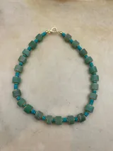 Collar de cuentas de piedra natural en tonos verde y lila, intercaladas con cuentas turquesas y detalles dorados.
