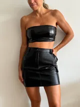 Minifalda negra de cuero sintético con textura de piel de cocodrilo, corte ajustado, tiro alto, bolsillos laterales tipo cargo y cierre frontal con botón y cremallera.