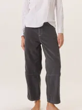 Pantalón de pana color gris oscuro, de corte barrel (holgado en caderas y muslos, ligeramente afín hacia el tobillo). Presenta costuras visibles en contraste de color amarillo claro, especialmente en la zona de la rodilla y el ruedo.