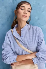 Camisa de rayas blancas y azules con cuello mao decorado con volados sutiles, cierre frontal de botones y mangas largas.