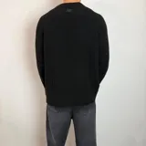 Sweater de tejido de punto grueso color verde militar, con cuello redondo y mangas largas tipo raglán. Presenta un corte holgado y una pequeña etiqueta con logo en el puño.