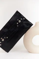 Sobre de cuero negro con solapa, cierre magnético y muñequera con tachas plateadas.