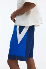 Short de baño y deportivo confeccionado en nylon, de corte holgado. Presenta un diseño de bloques de color en tonos azul, azul marino y blanco. Cuenta con cintura elástica con cordón ajustable blanco, bolsillos laterales y aberturas en los costados del ruedo. Incluye suspensor interno de malla.