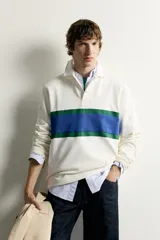 Remera polo de manga larga de corte regular fit, confeccionada en algodón color blanco crudo. Presenta cuello solapa blanco, cierre frontal con botonadura oculta y una franja horizontal ancha en el pecho en color azul y verde.