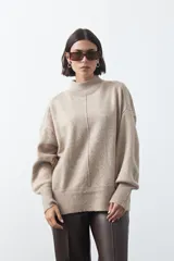 Polera de tejido de punto color gris, con cuello alto, mangas largas abullonadas con puños elásticos y costura central vertical en el frente. Presenta una abertura sutil en la espalda.