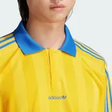 Camiseta de manga larga Adidas Originals, de corte holgado y color amarillo con rayas verticales sutiles en tono más oscuro y detalles en azul en cuello polo, puños y las clásicas franjas en las mangas. Cuenta con el logo bordado en el pecho.