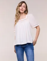 Blusa de corte holgado color marfil, confeccionada en mezcla de modal y algodón, con escote cuadrado y mangas cortas adornadas con detalles de puntilla calada.