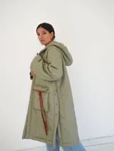 Abrigo largo color marrón con diseño acolchado de rombos, capucha y cierre frontal con botones a presión. Tiene bolsillos laterales y aberturas en los laterales inferiores.