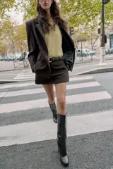 Falda pantalón corta de tiro medio color beige claro, con cierre frontal y detalle de cinturón negro con hebilla metálica redonda dorada.