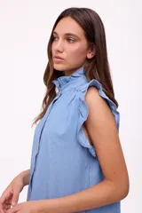 Blusa celeste de denim con cuello mao con volados, mangas cortas con volados y cierre frontal con botones.