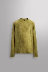 Camiseta térmica de manga larga ranglán, cuello redondo, color verde oliva con efecto tie-dye o jaspeado. Presenta tejido con lana, alta elasticidad y ajuste al cuerpo, con estructuras combinadas para facilitar la transpiración y sin costuras.
