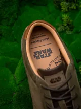 Zapatillas urbanas de edición limitada inspiradas en Star Wars, color verde oliva con detalles en marrón. Presentan una combinación de cuero y descarne, con el rostro de Yoda grabado en el lateral y el logo de Star Wars en la lengüeta.