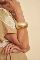Brazalete ancho dorado con textura estriada y acabado brillante.