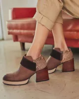 Botinetas de cuero con diseño combinado. Presentan puntera y lateral en cuero liso marrón, una banda central en gamuza oscura y talón con textura de reptil. Incluyen plataforma y taco cuadrado de madera, con cierre lateral.