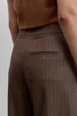 Pantalon de vestir de corte wide leg, color marrón con estampado de rayas diplomáticas finas. Presenta cintura alta, bolsillos laterales y cierre frontal.
