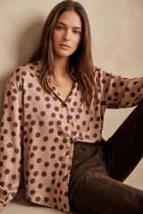 Camisa oversize de poliéster color rosa con estampado de lunares marrón oscuro, cuello camisero, cierre frontal de botones y mangas largas con puños elásticos.