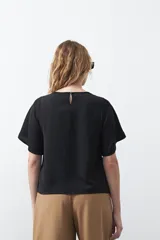 Top negro de manga corta con detalle de nudo en el escote y abertura tipo gota. Presenta una silueta relajada y textura sutil en la tela.