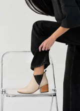 Botinetas de cuero color beige claro con inserciones elásticas laterales en negro y taco cuadrado de madera. Presentan punta fina y tirador trasero.