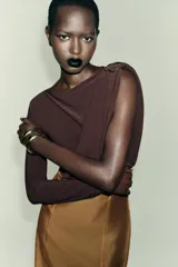 Body de manga larga color marrón oscuro, con escote asimétrico drapeado y detalle de broche metálico en el hombro derecho.