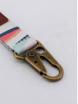 Llavero con cinta de tela estampada con formas geométricas en tonos pastel, detalles en cuero sintético marrón y herrajes metálicos color bronce.