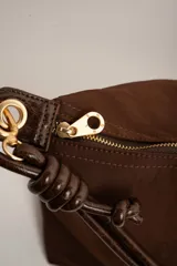 Cartera tipo shopper color marrón, con solapa frontal decorativa en tono más oscuro y tiras con nudos. Incluye herrajes dorados y un charm colgante con cuentas de madera.