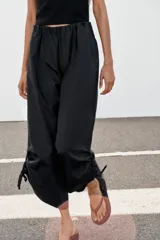 Pantalón culotte de tiro medio, color verde militar, con cintura elástica y bolsillos laterales ocultos. Presenta un diseño de bajo ancho con aberturas ajustables mediante cordones fruncidos en los laterales.