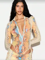 Vestido largo de silueta ajustada con estampado de piel de serpiente en tonos cálidos. Presenta escote profundo con cuello tipo camisa, mangas largas y recortes laterales cut-out que estilizan la figura.