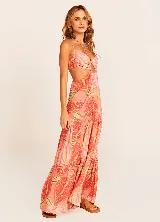 Vestido largo de tirantes finos con estampado de hojas en tonos coral, naranja, verde y amarillo. Presenta escote en V con detalle de nudo y aberturas en los laterales de la cintura.