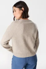 Saco tipo cardigan de punto color crudo, con cuello redondo, cierre frontal de botones y mangas largas con puños acanalados.