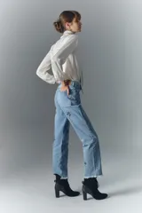 Jean de tiro alto en denim azul rígido, con lavado localizado, bigotes y apliques de estrellas brillantes. Presenta pierna recta y ruedo desflecado.