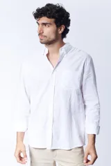 Camisa blanca de lino, de corte clásico, con cuello abotonado, manga larga con puños abotonados y bolsillo en el pecho.