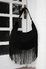 Bolso tipo hobo de gran tamaño confeccionado en gamuza negra, con diseño de flecos largos en la parte inferior y asa con detalles de costuras artesanales.