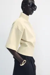 Jersey de punto color amarillo claro, con cuello subido, manga corta con hombreras y cintura entallada.