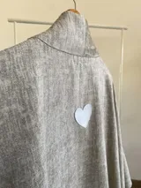 Ruana de diseño estructurado confeccionada en tela tipo tapiz, con solapas amplias y caída fluida. Presenta un tono neutro con textura sutil y acabado reversible en un tono más claro.