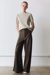Pantalón de tiro alto confeccionado en tejido efecto piel, con diseño de pierna ancha y costuras marcadas en el delantero. Presenta cintura con trabillas, cierre frontal con cremallera, botón y gancho metálico, y bolsillos de plastrón en la espalda.