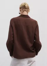 Camisa de manga larga con cuello camisero, cierre frontal de botones, bolsillo de parche en el pecho y diseño recto.