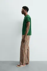 Camiseta de corte relajado, color verde, con cuello redondo y manga corta. Presenta un texto bordado en relieve con letras amarillas y contorno oscuro en el centro del pecho.
