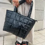 Bolso tote negro con diseño acolchado y cierre de cremallera. Tiene dos asas de hombro y un bolsillo frontal con cierre.