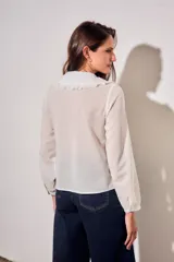 Blusa blanca de algodón peinado con mangas largas, cuello babero bordado y pliegues frontales.