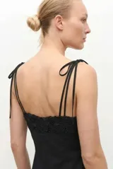Vestido midi negro con tirantes ajustables mediante lazos, escote recto y detalle de encaje bordado en el pecho y en el ruedo.