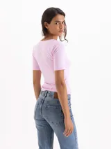 Top de silueta ajustada y largo hasta la cadera, confeccionado en tejido de punto liso color rosado. Presenta un escote ovalado profundo y mangas cortas de calce ceñido.