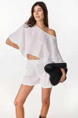 Blusa de lino italiano color blanco, con diseño holgado, escote asimétrico estilo off-shoulder y mangas cortas amplias.