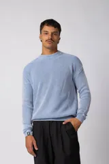 Sweater de punto con textura waffle en color celeste y blanco, de corte relajado, cuello redondo y manga larga con puño elástico que incluye una etiqueta decorativa.