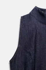 Vestido corto de denim azul oscuro, sin mangas, con cuello alto y cierre de cremallera en la espalda. Presenta costuras contrastantes en color claro a lo largo del cuerpo.