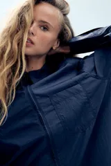 Camisa oversize de nylon color azul marino, con cuello solapa, manga larga, bolsillo de parche en el pecho y cierre frontal con cremallera.