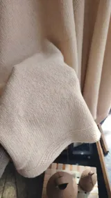 Ruana de lana color beige, con diseño abierto, caída envolvente y terminaciones acanaladas en los bordes.