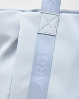 Cartera tipo tote color celeste, con asas de hombro y tiras frontales con la inscripción de la marca en relieve. Cuenta con un pequeño aplique circular con el logo en el centro.