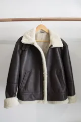 Campera tipo bomber de cuero genuino color negro, con interior y cuello de piel sintética negra. Presenta cierre frontal metálico, bolsillos laterales y puños con terminación en tejido acanalado.
