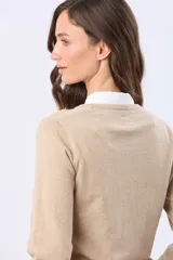 Buzo tejido en hilo de algodón color beige, con cuello redondo y manga larga. Presenta un corte clásico y un pequeño detalle metálico en la parte inferior izquierda.